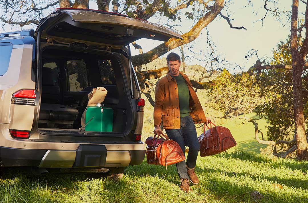 The owner of the Lexus GX takes his bags out of the boot of the GX, surrounded by greenery. 