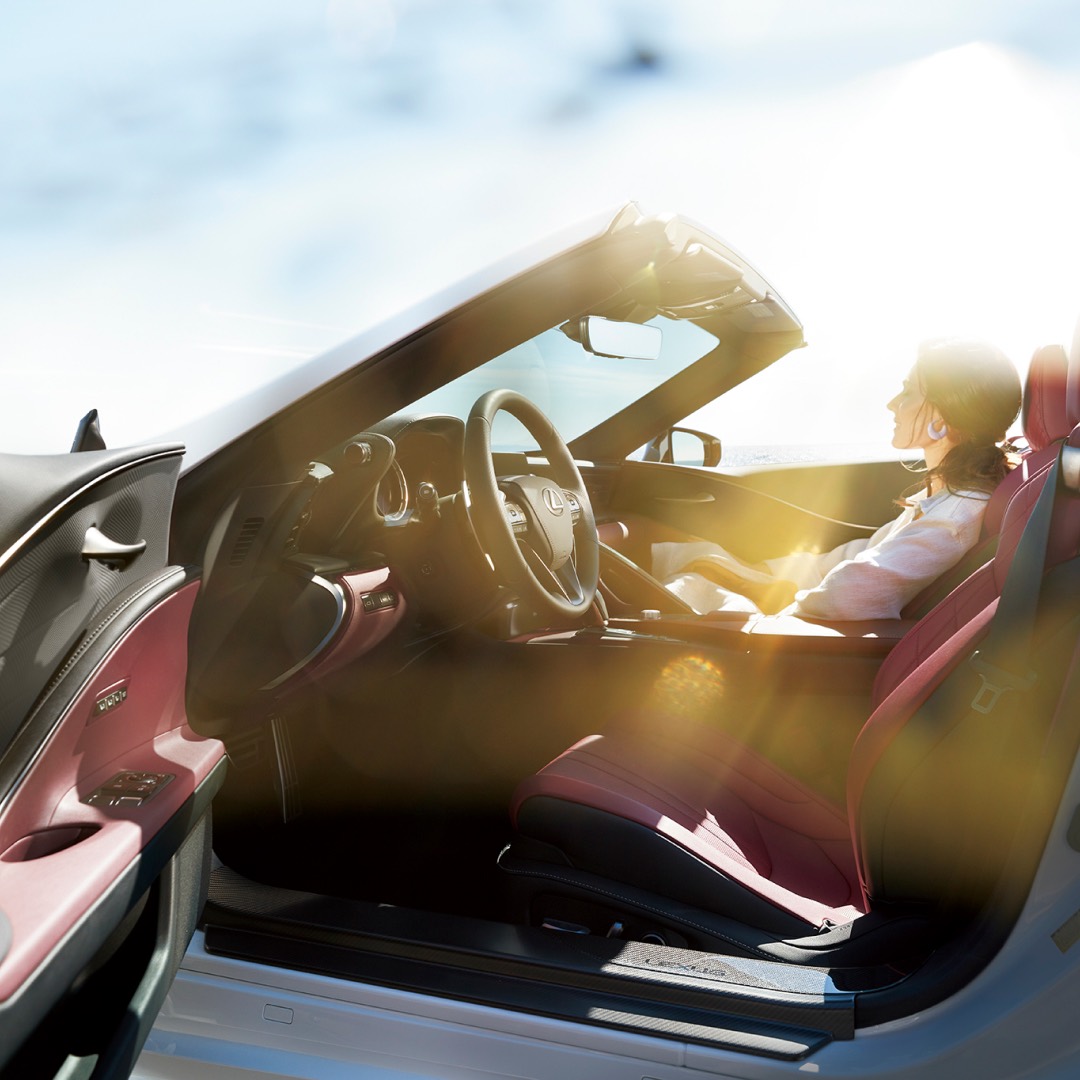 Low, wide angle view of the driver's side of an LC Convertible, as a lady sits in the passenger seat. The sun is shining.