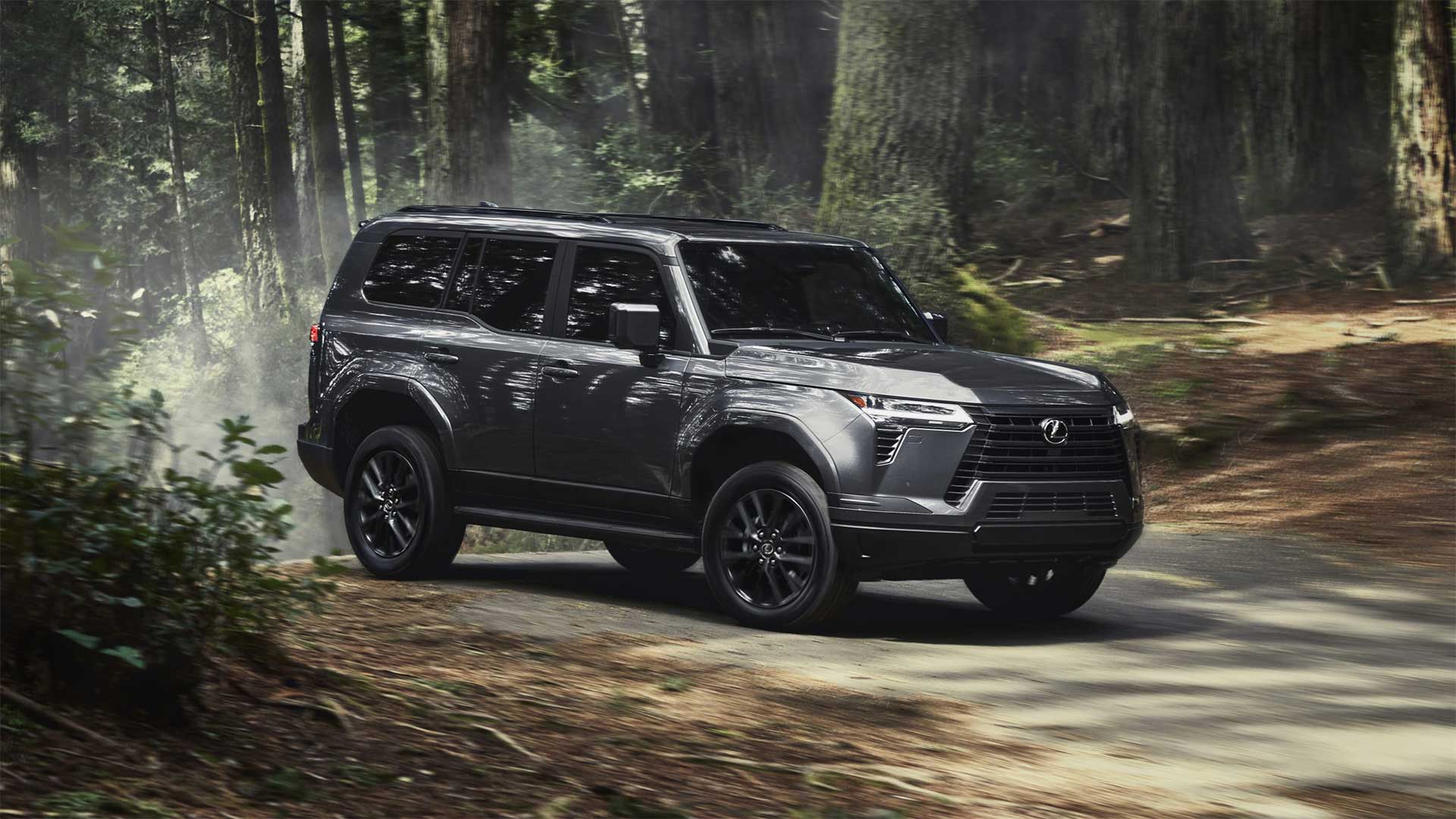 Lexus GX drives on a dusty country road with the trunks of large trees in the background.