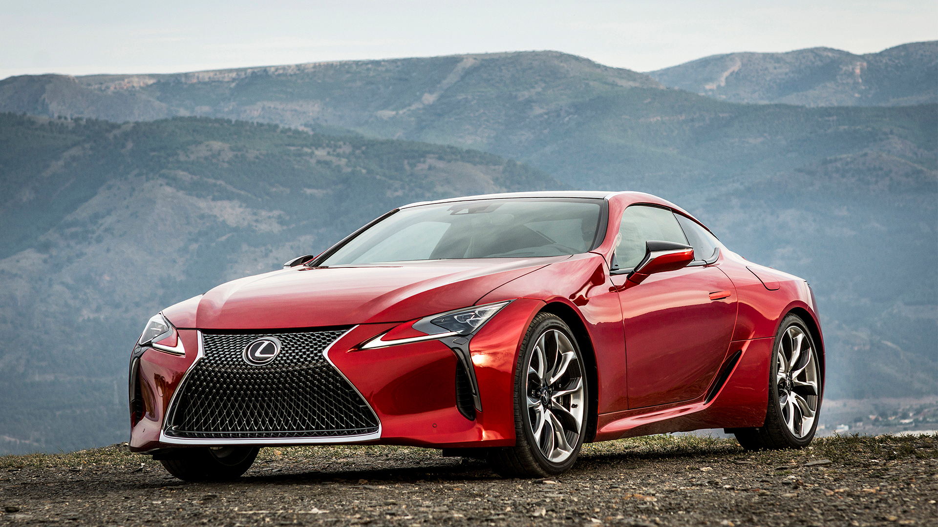 A red LC 500 coupe parked on gravel with mountains in the background