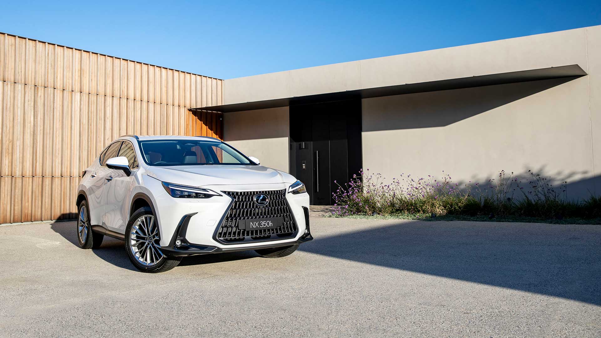 A white Lexus NX 350h parked in a driveway of a modern home.