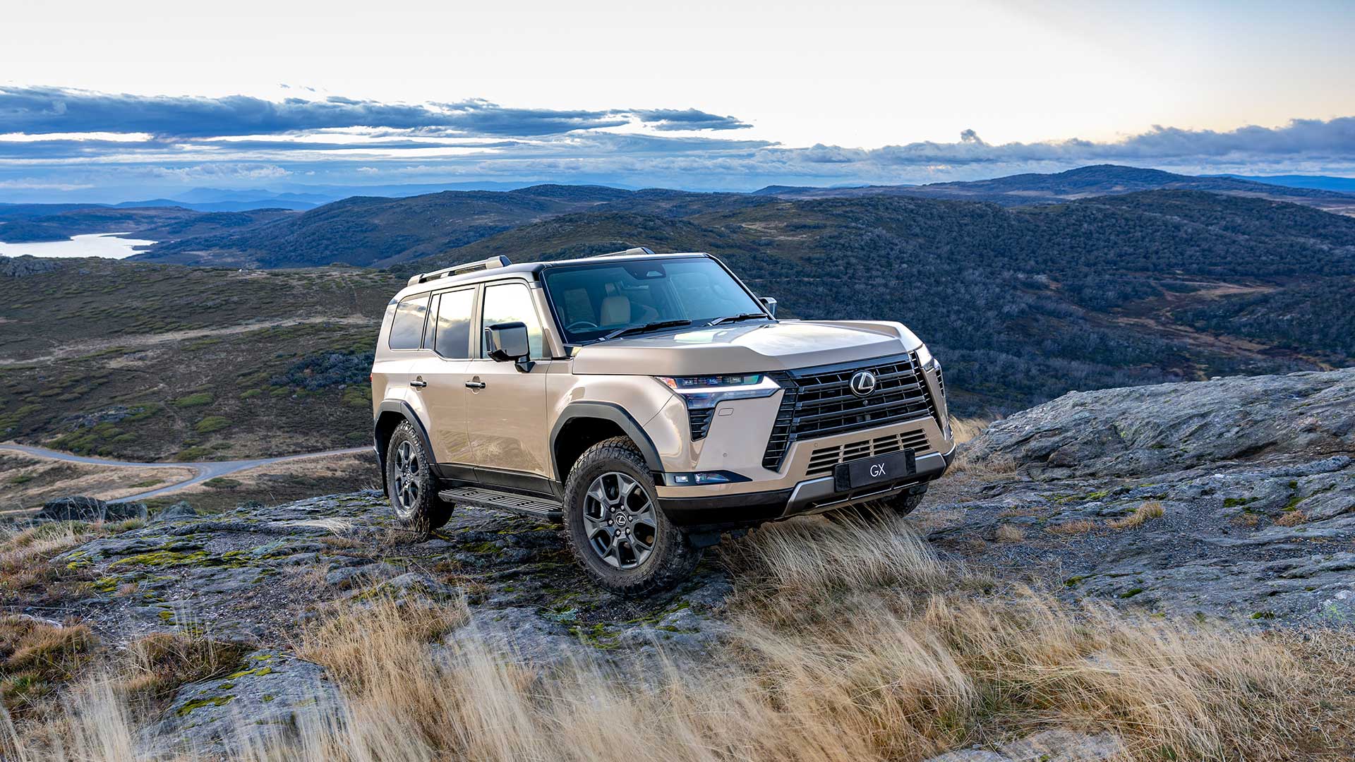 An Earth coloured Lexus GX driving cross country over rocky terrain with mountains in the background