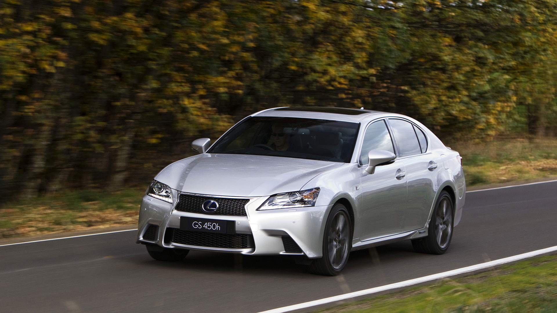Silver Lexus GS 450h drives along a road with green trees in the background