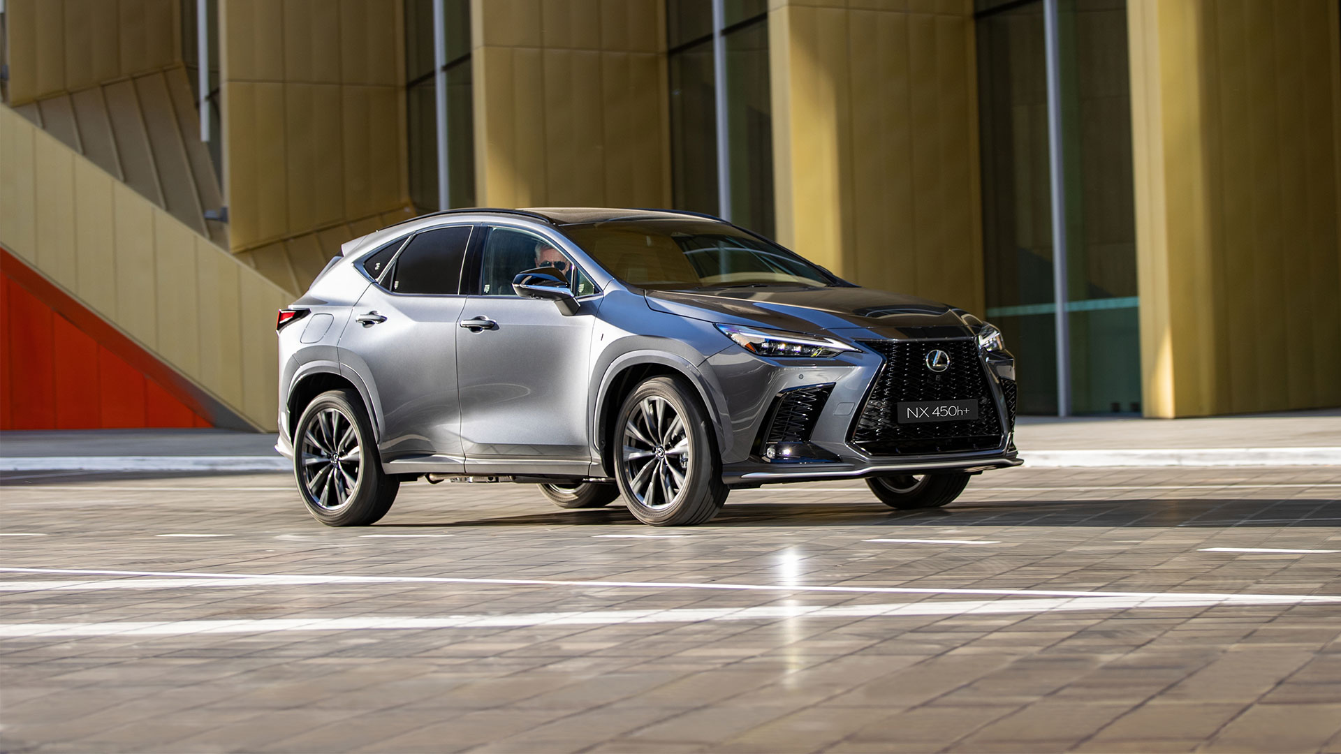 A Lexus NX 450h+ parked on a pavement with a yellow building in the background