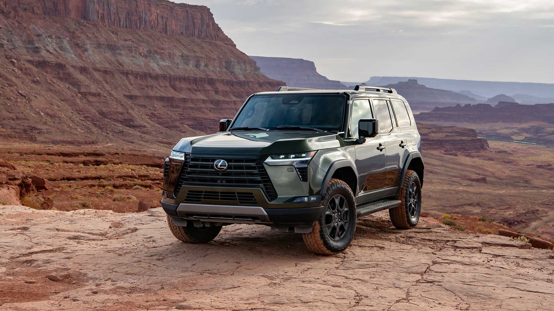 The dark grey Lexus GX parked on a red cracked ground with mountains in the background