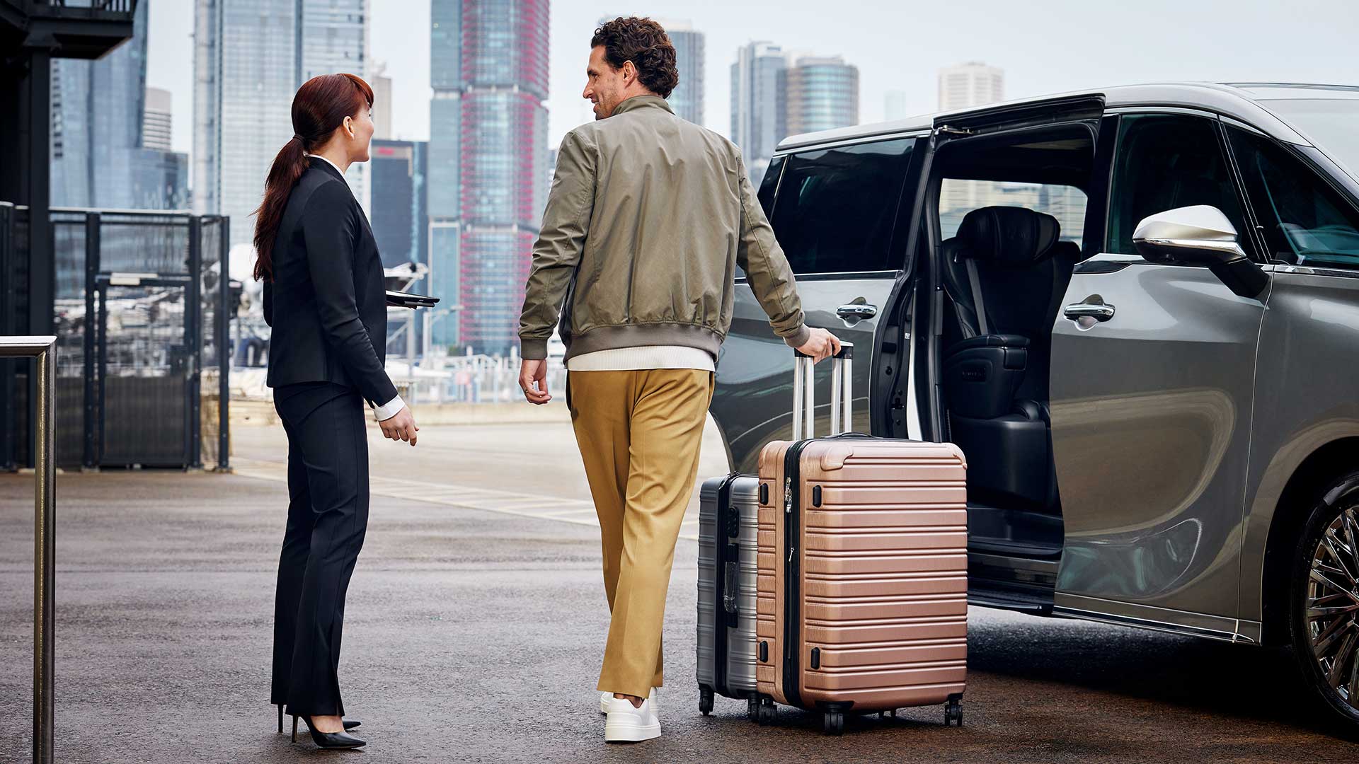 Two people with a suitcase entering a grey Lexus LM vehicle