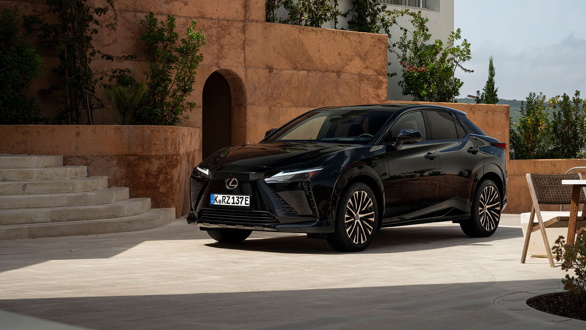 Black Lexus RZ electric SUV parked in a modern architectural courtyard with stone walls and greenery