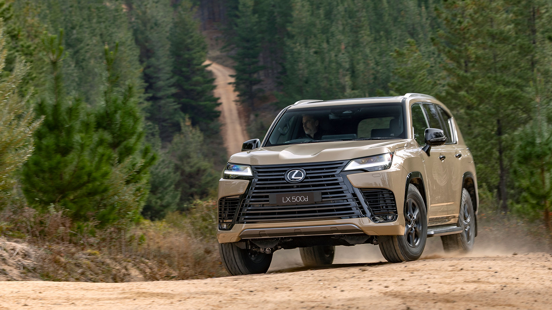 The Lexus LX 500d Overtrail in Earth tone driving on a dirt road surrounded by trees